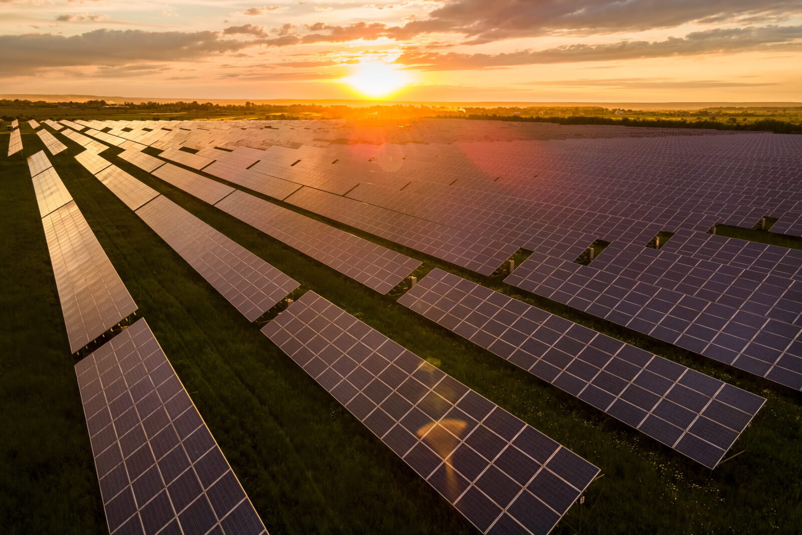 Sunset over a vast field of solar panels arranged in neat rows, reflecting golden light across the farm numerically.