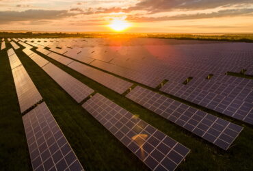 Sunset over a vast field of solar panels arranged in neat rows, reflecting golden light across the farm numerically.