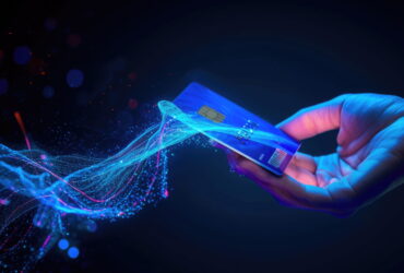 Hand holding a blue credit card with a chip, surrounded by glowing blue digital particles and light streaks.
