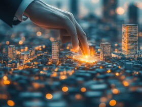 A hand touches a glowing miniature city model, highlighting illuminated skyscrapers as part of urban planning or smart cities concept.