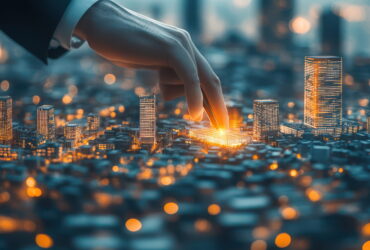 A hand touches a glowing miniature city model, highlighting illuminated skyscrapers as part of urban planning or smart cities concept.