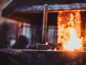 Metal rod resting on an anvil with bright orange forge flames in the background, blacksmithing scene
