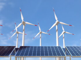 Solar panels in the foreground with wind turbines in the background under a clear blue sky
