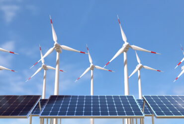 Solar panels in the foreground with wind turbines in the background under a clear blue sky
