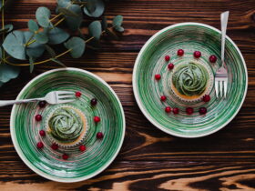 Top-down view of green-striped plates holding a matcha swirl dessert with scattered red berries on a dark wooden table, with cutlery nearby and eucalyptus on the side.”,