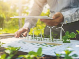 Person outdoors reviewing documents with a scale model of wind turbines on a table surrounded by greenery.