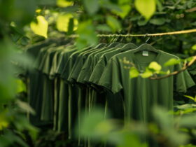 Rows of green T-shirts hanging on a rack outdoors among lush green plants.