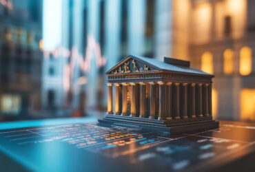 Bronze miniature classical temple model on a dark desk with blurred city lights in the background.
