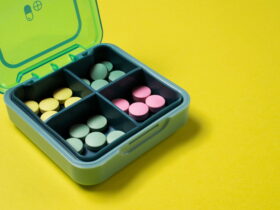 Open turquoise pill organizer with pastel yellow, green, and pink pills in its compartments on a bright yellow background moment
