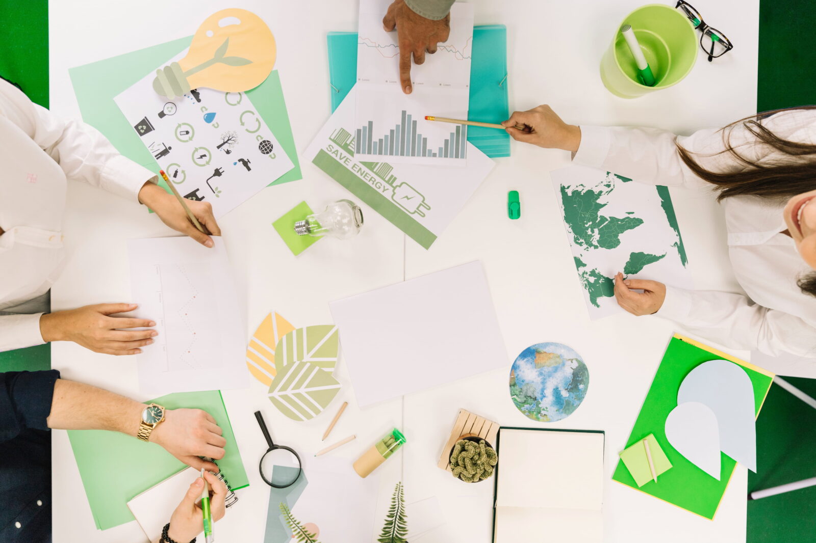 Top-down view of people around a white table working on environmental charts and illustrations.