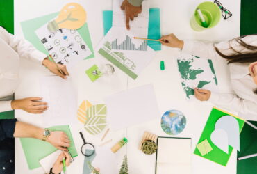Top-down view of people around a white table working on environmental charts and illustrations.