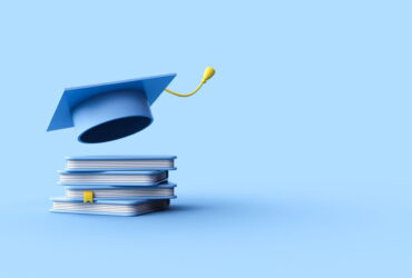 Blue graduation cap perched on a stack of textbooks against a blue backdrop, symbolizing education and achievement.