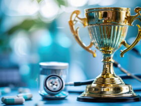 Gold trophy on a blue medical workspace, with a stethoscope and scattered pills in the foreground, symbolizing achievement in healthcare.