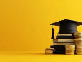 Graduation cap on a stack of books with coin stacks beside it against a yellow backdrop, symbolizing education and funding